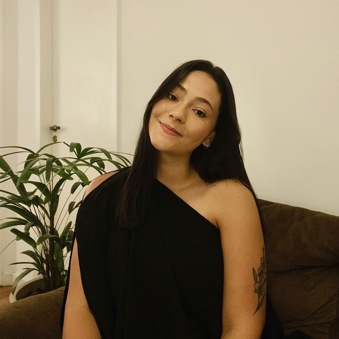 Luiza Soares, psicóloga, sentada em um sofá ao lado de uma planta, sorrindo
